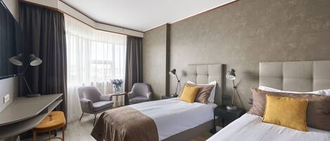 Une chambre d’hôtel moderne équipée de deux lits, d’un bureau, d’une chaise et d’une petite table avec une lampe.