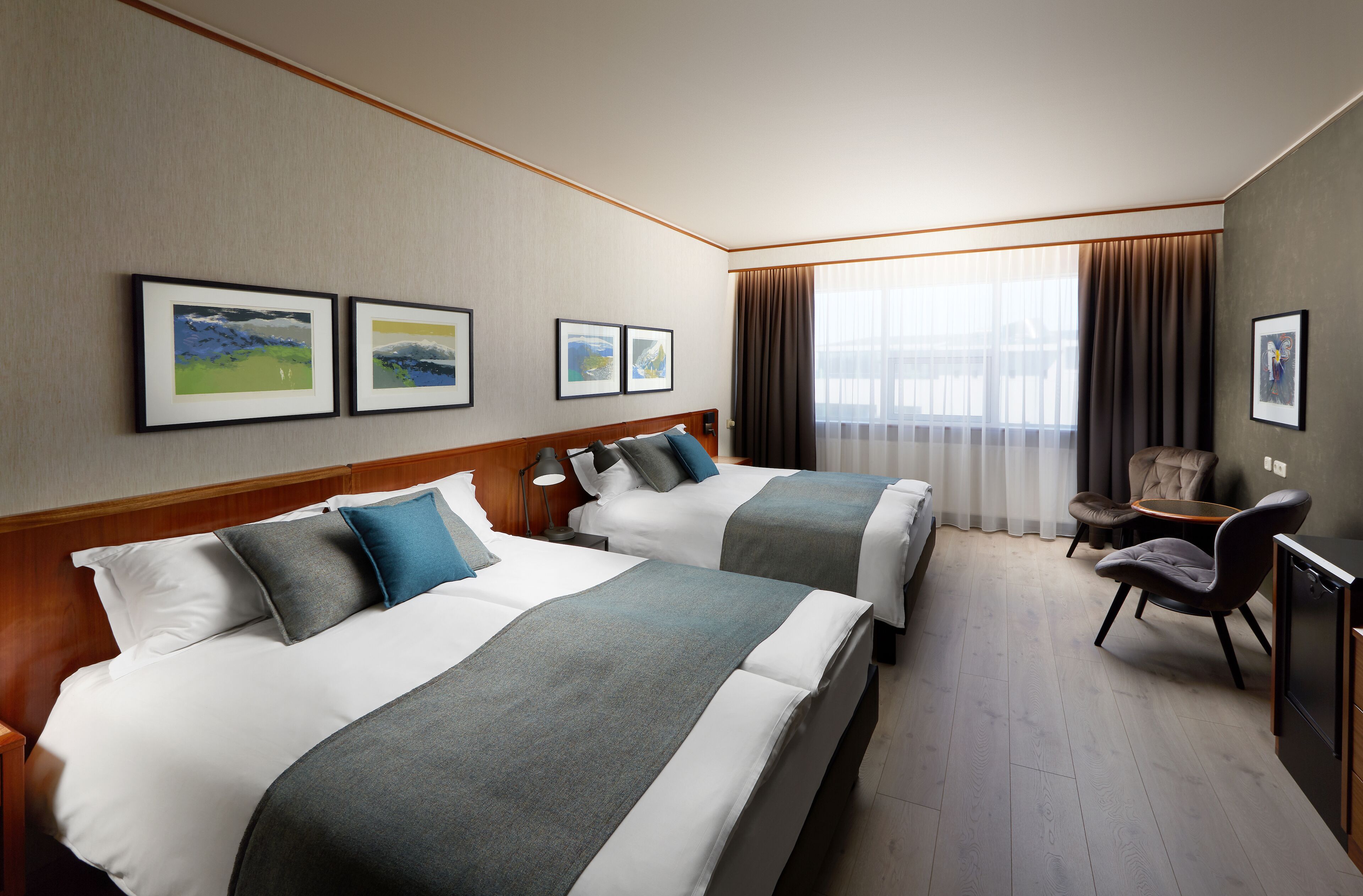 A hotel room with two beds, a desk, a chair, and a large window with curtains.