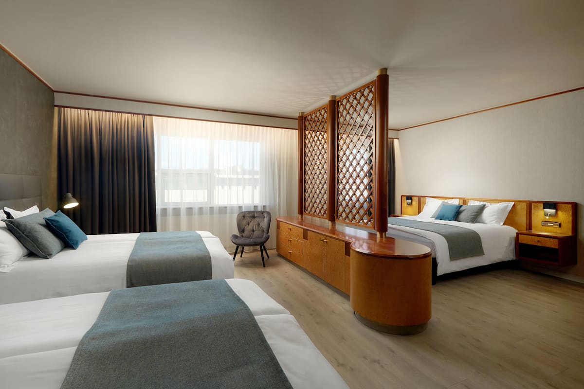 Ein Hotelzimmer mit zwei Betten, einem Schreibtisch, einem Stuhl und einem großen Fenster mit Vorhängen.