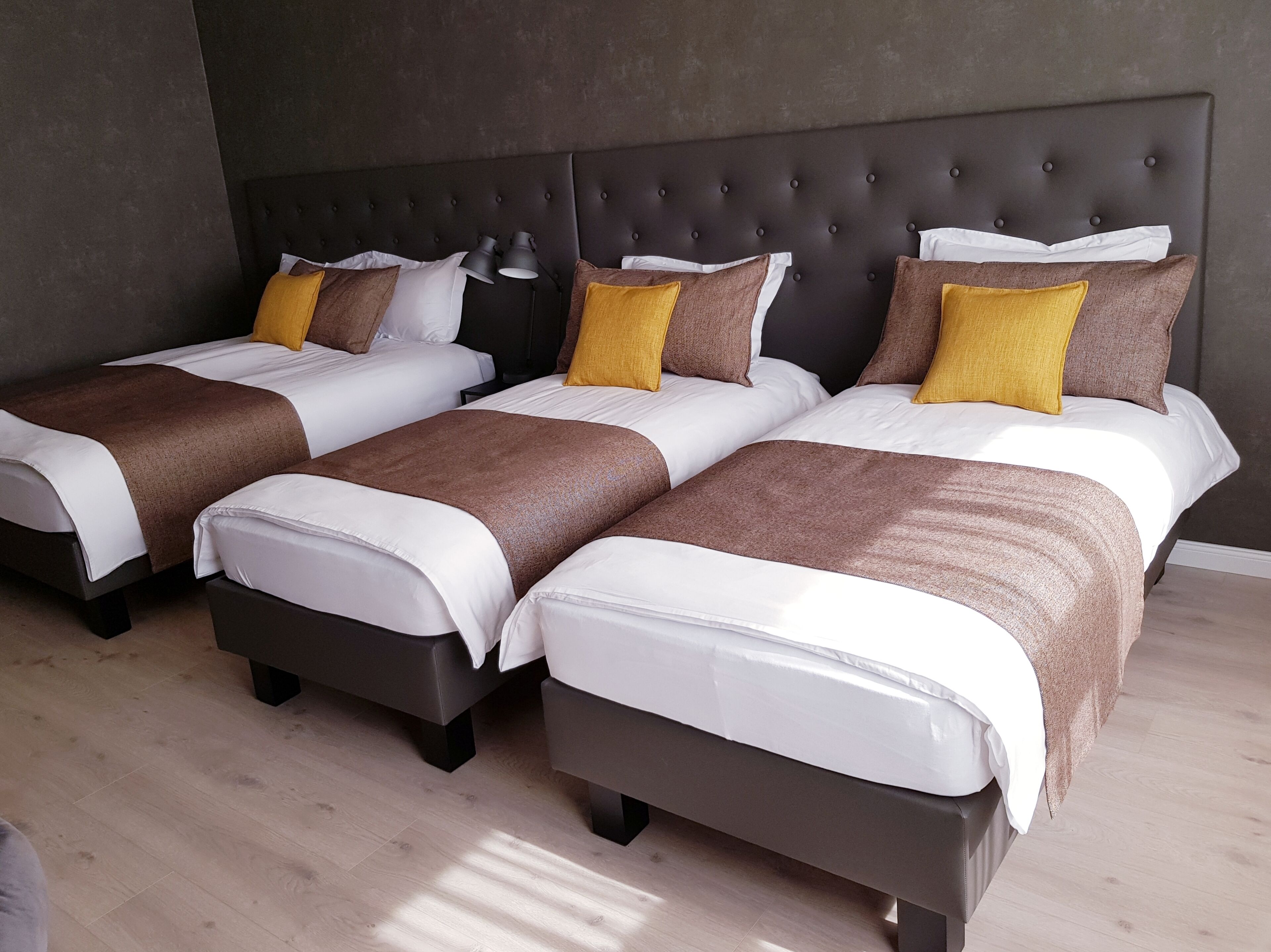A hotel room with three beds, each with a brown headboard, white bedding, and a yellow accent pillow.