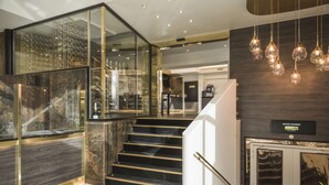 A modern hotel lobby with a glass-enclosed wine cellar, a staircase with a handrail, and a reception desk with a welcome sign. - Radisson Blu Limfjord Hotel Aalborg (Aalborg)