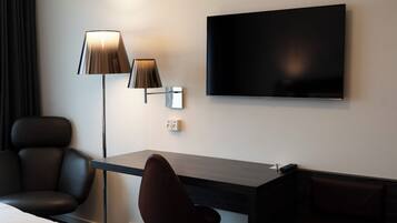 A hotel room with a desk, two chairs, a TV, and a lamp.