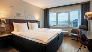 A hotel room with a large bed, a desk, a chair, a view of the city, and a wall with a cityscape mural. - Radisson Blu Limfjord Hotel Aalborg (Aalborg)