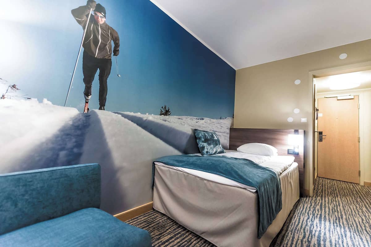 Quarto de hotel com uma cama, um sofá azul, um mural na parede com um esquiador e uma porta.