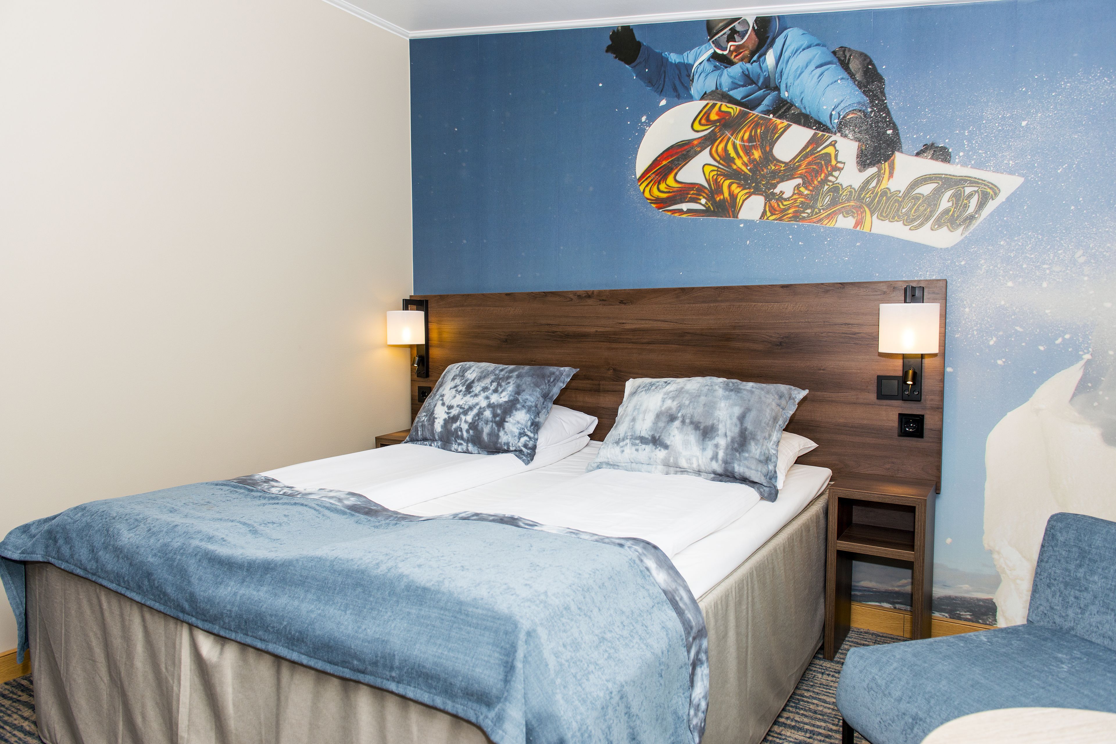 A hotel room with a bed, two pillows, a nightstand, a lamp, and a wall mural of a snowboarder.