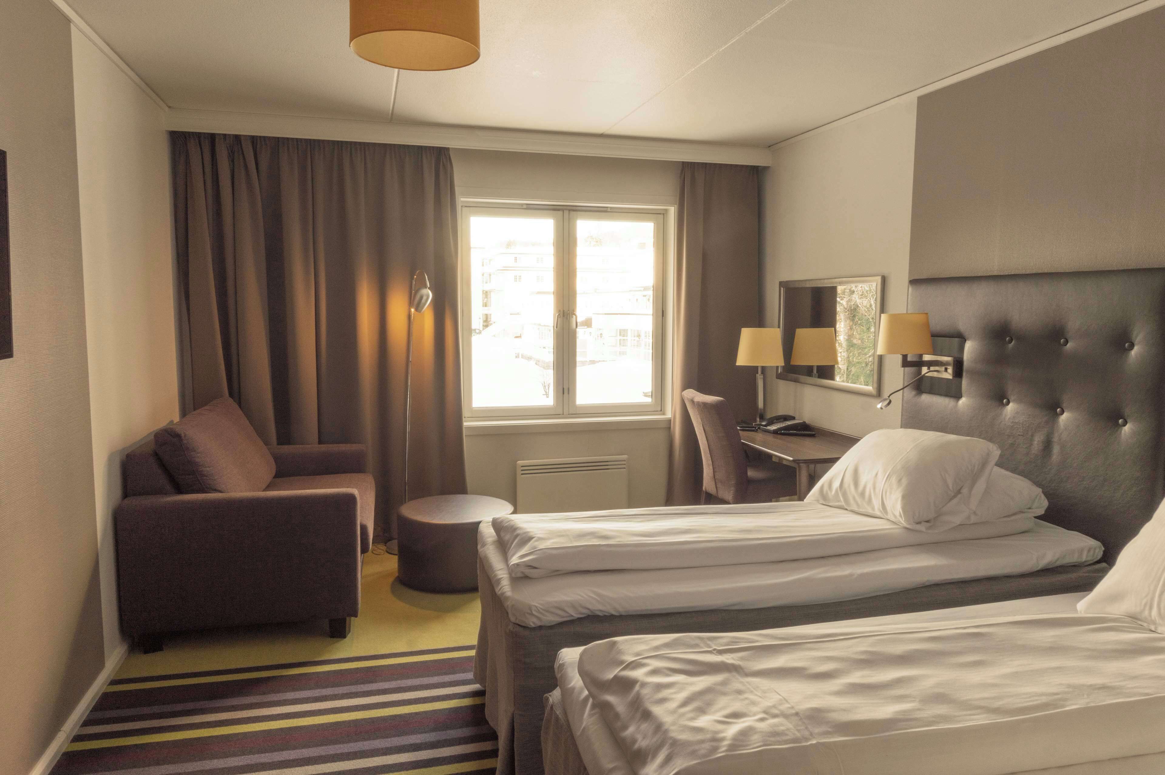 Quarto de hotel com duas camas, um sofá, uma escrivaninha e uma janela com cortinas.