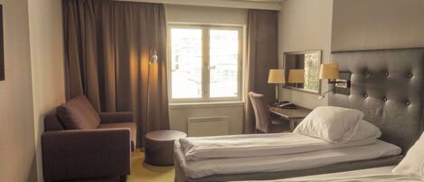 Quarto de hotel com duas camas, um sofá, uma escrivaninha e uma janela com cortinas.