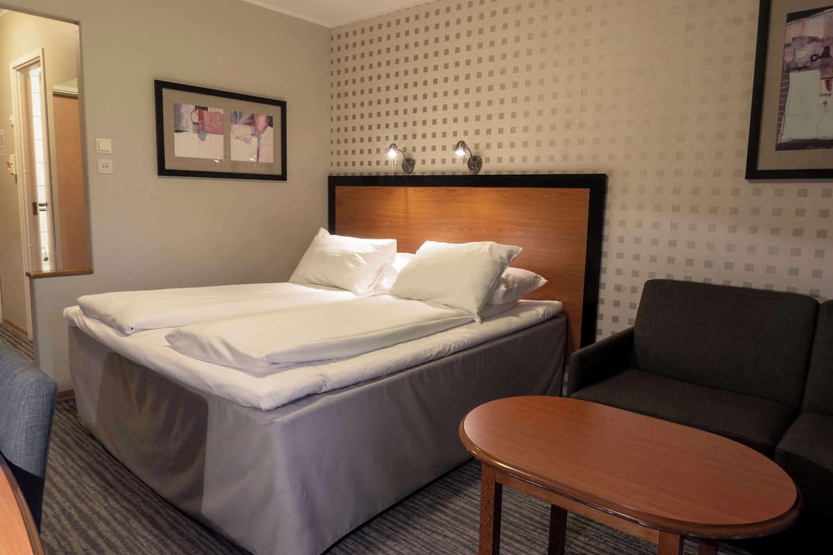 Quarto de hotel com cama de casal, uma mesinha, um sofá e um quadro na parede.