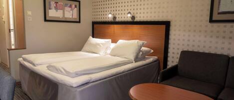 Una habitación de hotel con una cama doble, una mesita, un sofá y un cuadro enmarcado en la pared.