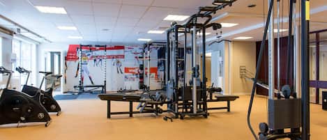 A gym with exercise equipment, treadmills, and a wall with posters.