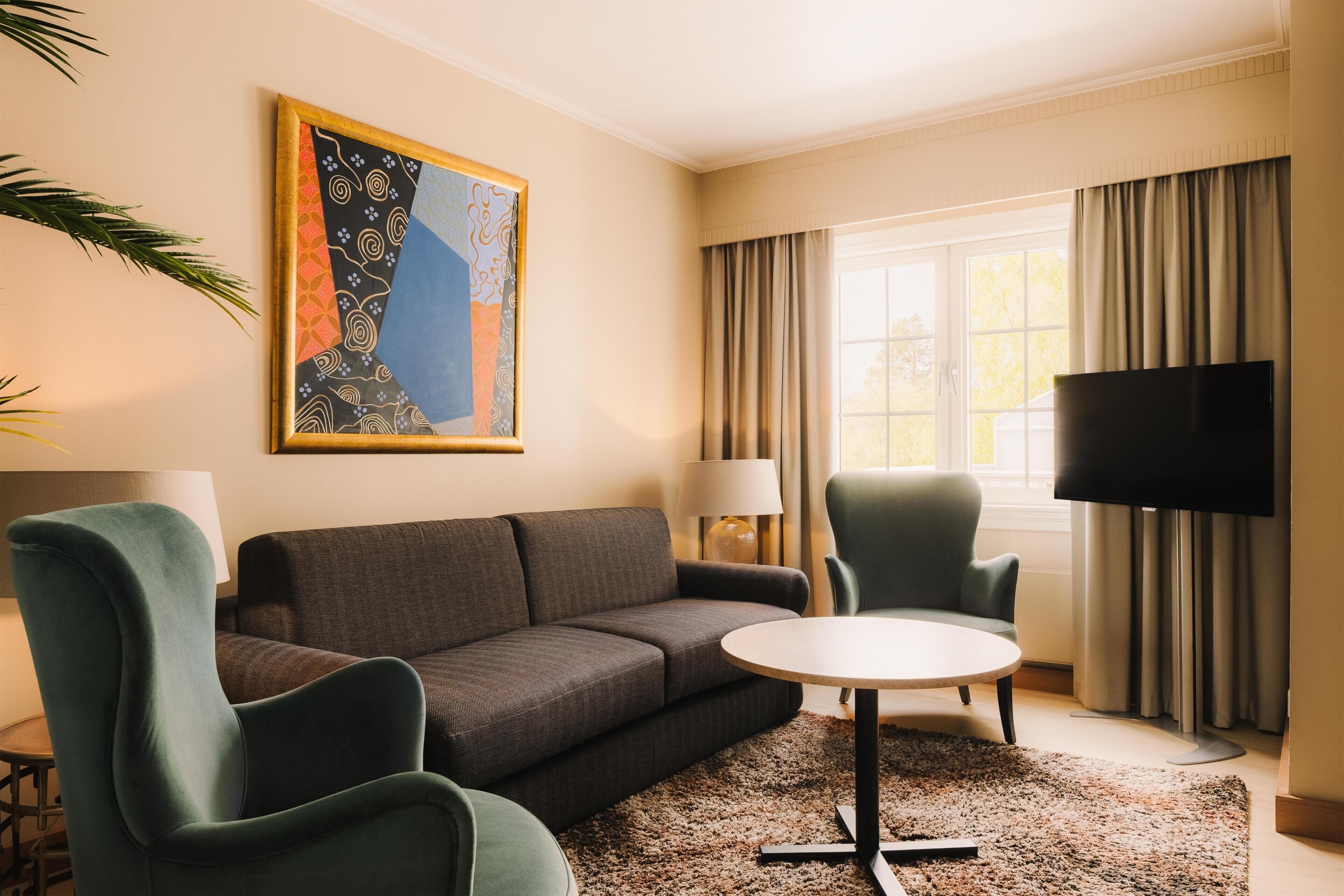 A living room with a sofa, two armchairs, a coffee table, a TV, and a painting on the wall.