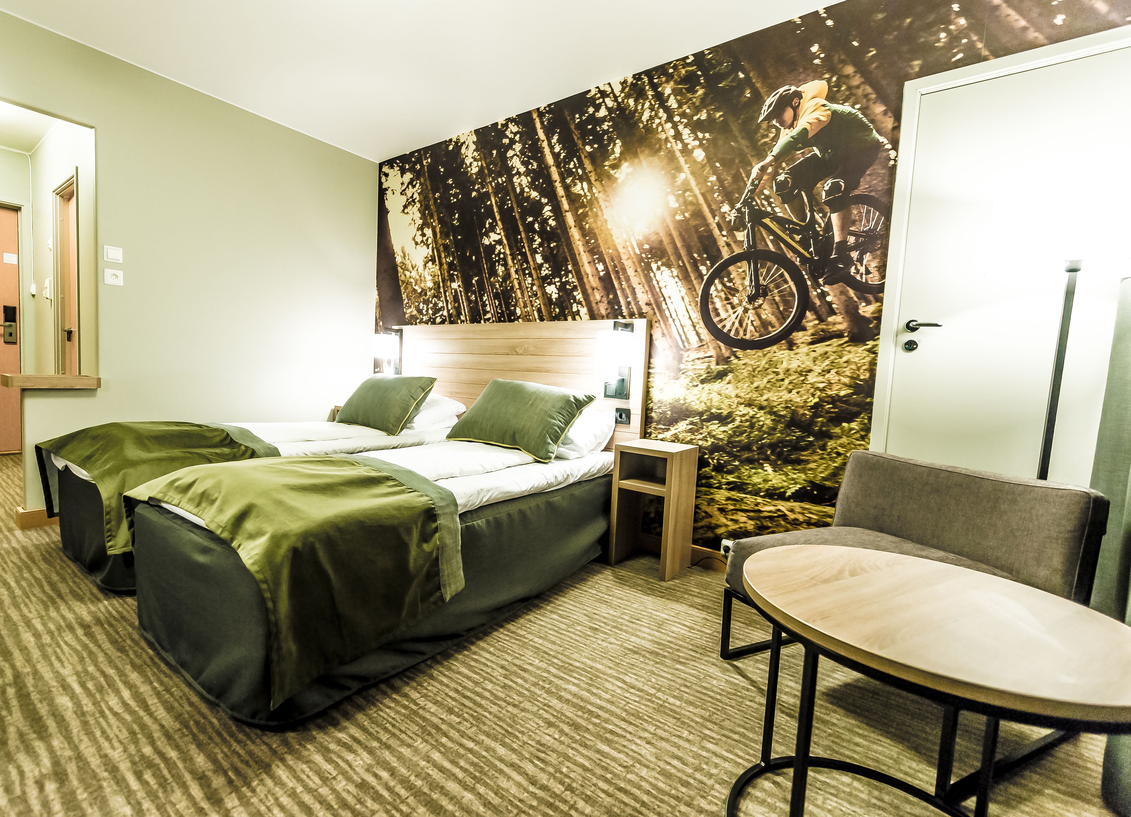 A hotel room with a bed, two bedside tables, a chair, and a large forest-themed wall mural.