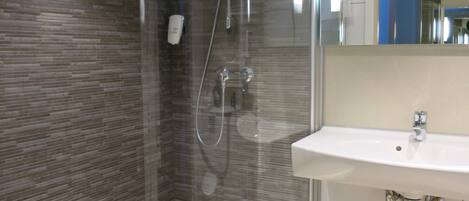 A modern bathroom with a glass-enclosed shower, a white sink, and a tiled floor.