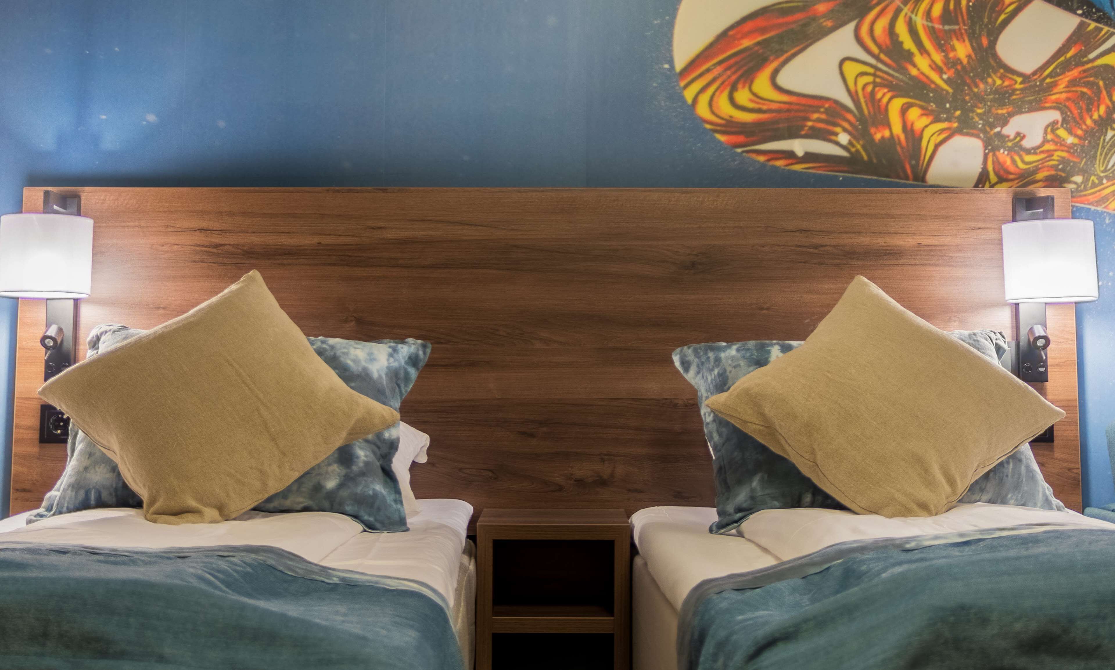 Una habitación de hotel con cabecera de madera, dos camas con almohadas a juego y un mural en la pared.