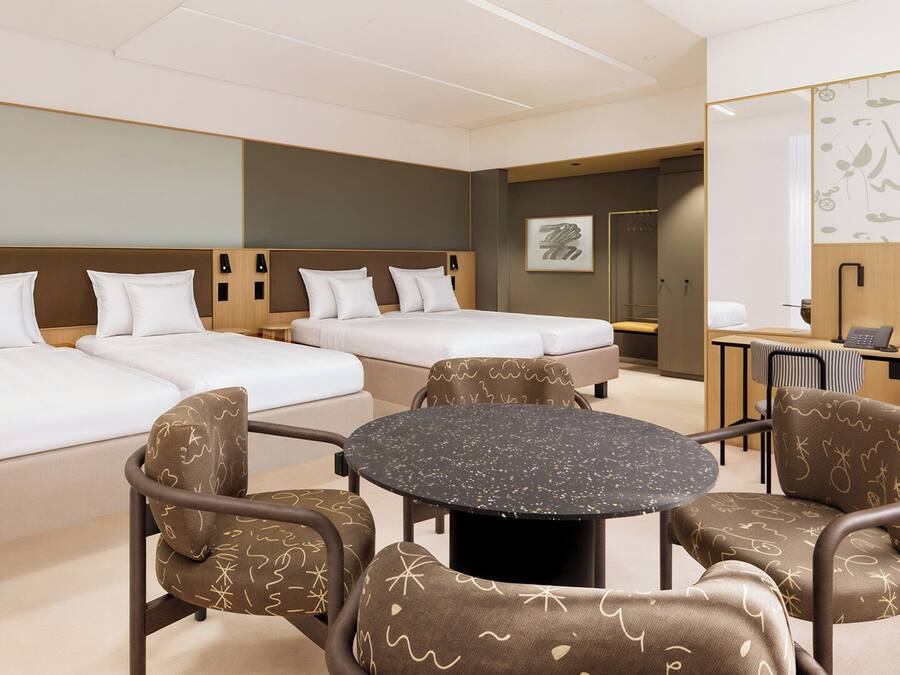 Quarto de hotel com duas camas, uma mesa redonda e quatro cadeiras.
