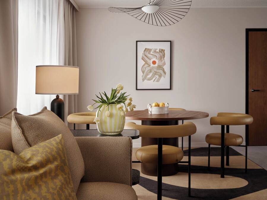 Una sala de estar moderna con un sofá, una mesa de comedor redonda con sillas, una lámpara y un florero con flores.