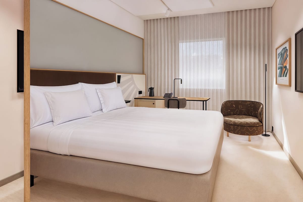 Une chambre d’hôtel avec un grand lit, un bureau, une chaise et un téléviseur fixé au mur.