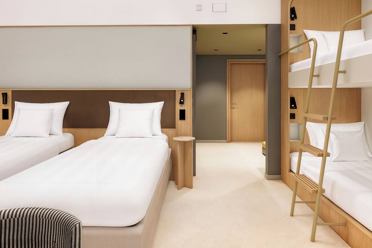 Une chambre d’hôtel avec deux lits simples, un lit superposé, une petite table ronde et une armoire.