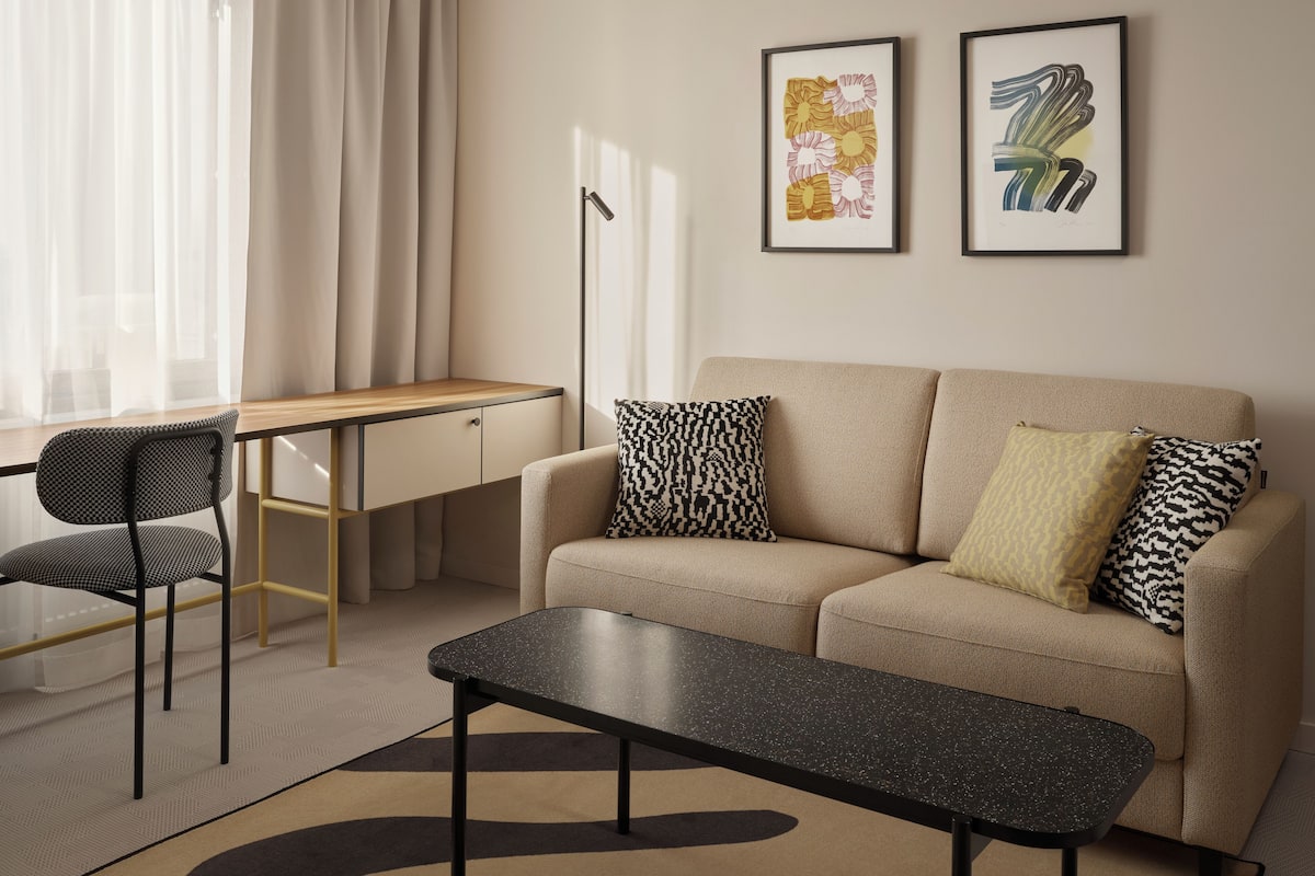 Un salon moderne comprenant un canapé, une table basse, un bureau et une chaise. Deux œuvres d’art encadrées sont accrochées au mur.