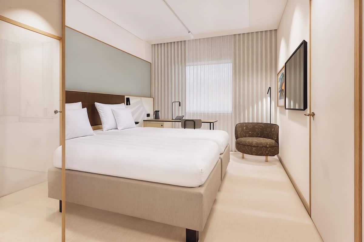 Habitació d'hotel moderna amb un llit gran, un escriptori, una cadira i un mirall gran.