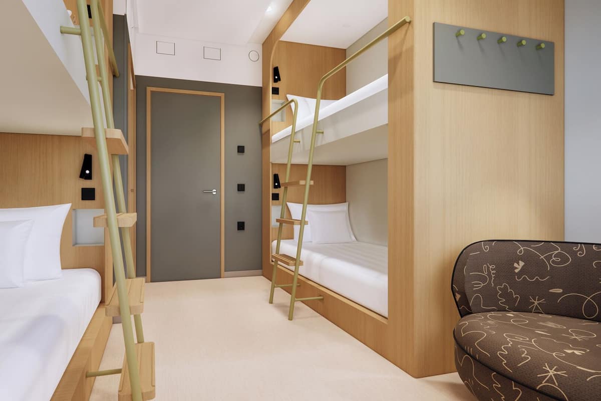 Une chambre d’hôtel compacte avec des lits superposés, un meuble mural en bois, un petit canapé et une porte donnant sur une autre pièce.