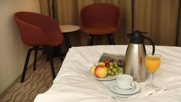 Un lit bien fait, avec un plateau de petit-déjeuner comprenant une assiette de fruits, une cafetière, un verre de jus d’orange et une tasse.