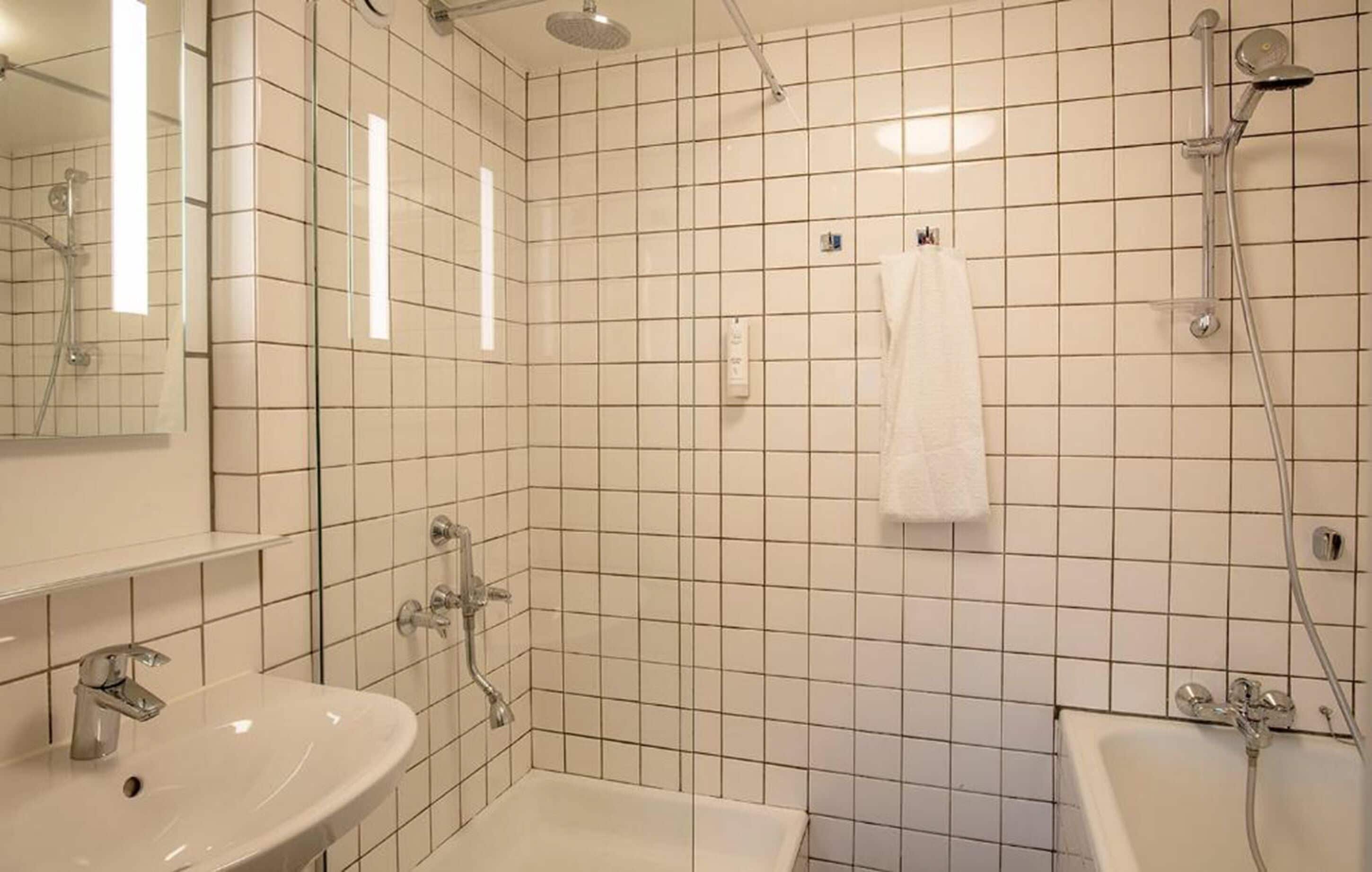 A bathroom with white tiled walls, a sink, a bathtub, and a shower.
