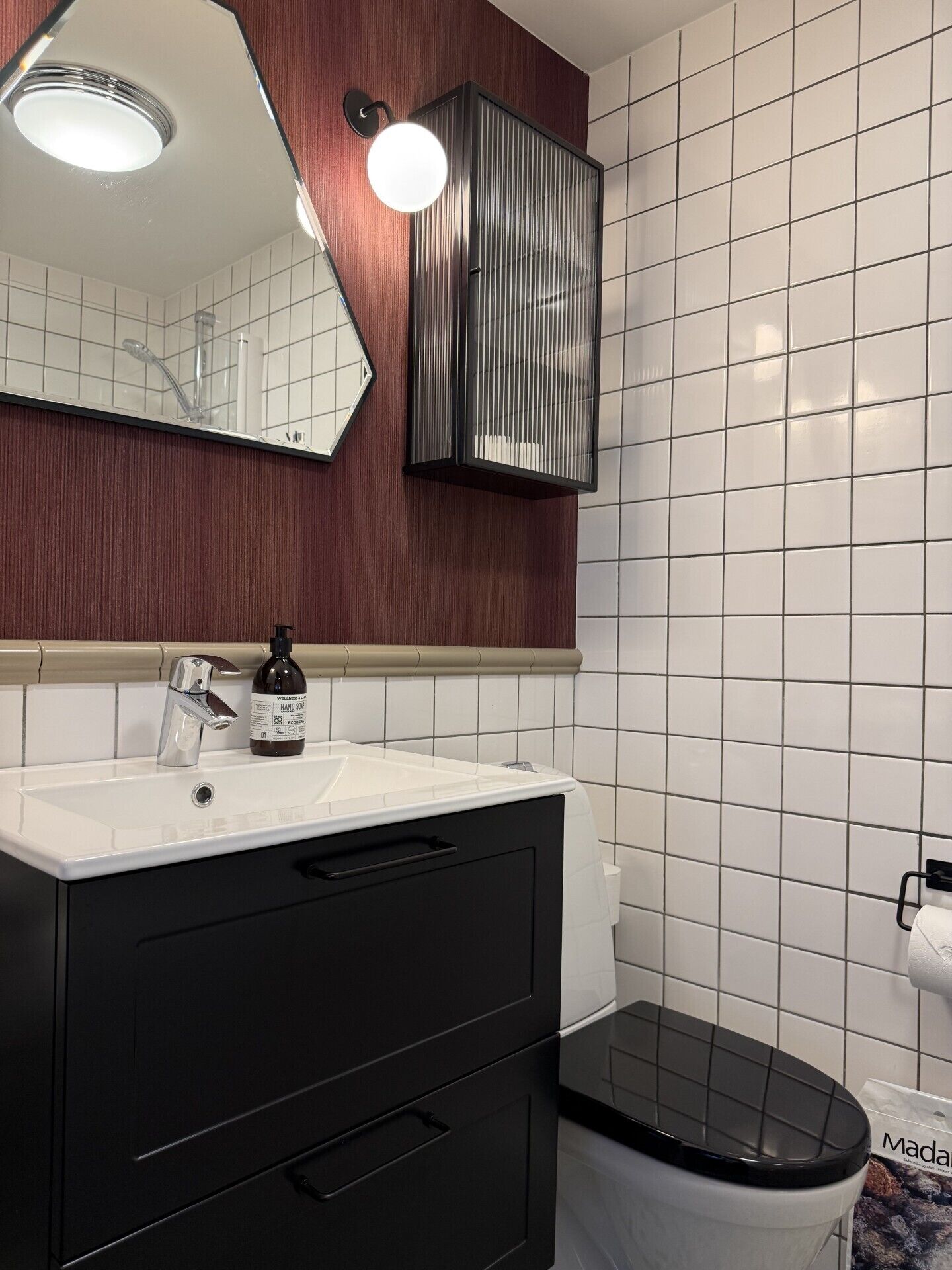 A bathroom with a white sink, black cabinet, and a mirror.