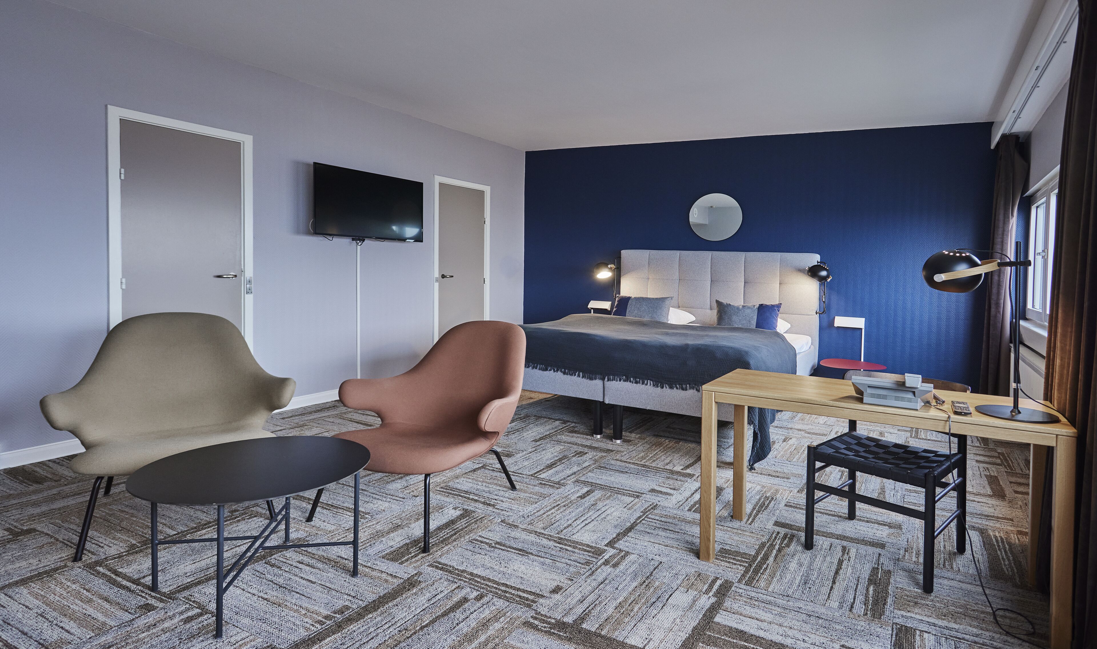 Un dormitorio moderno con cama, dos sillas, un escritorio, un televisor y una ventana con cortinas.