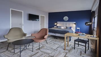 Un dormitorio moderno con cama, dos sillas, un escritorio, un televisor y una ventana con cortinas.