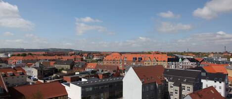 A high-rise building with a modern glass facade and a red-tiled roof, surrounded by traditional buildings with red roofs.