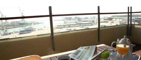 A balcony with a table set for breakfast, including a cup of coffee, a newspaper, a glass of orange juice, and a pastry.