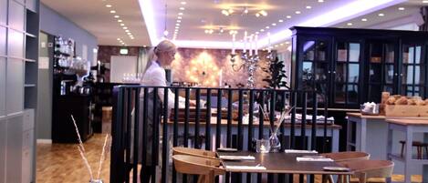 Un intérieur de restaurant moderne avec des tables et des chaises en bois, un bar et un plafond doté d’un éclairage encastré.