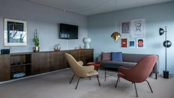 A modern living room with a sofa, two chairs, a coffee table, a TV, and artwork on the walls.