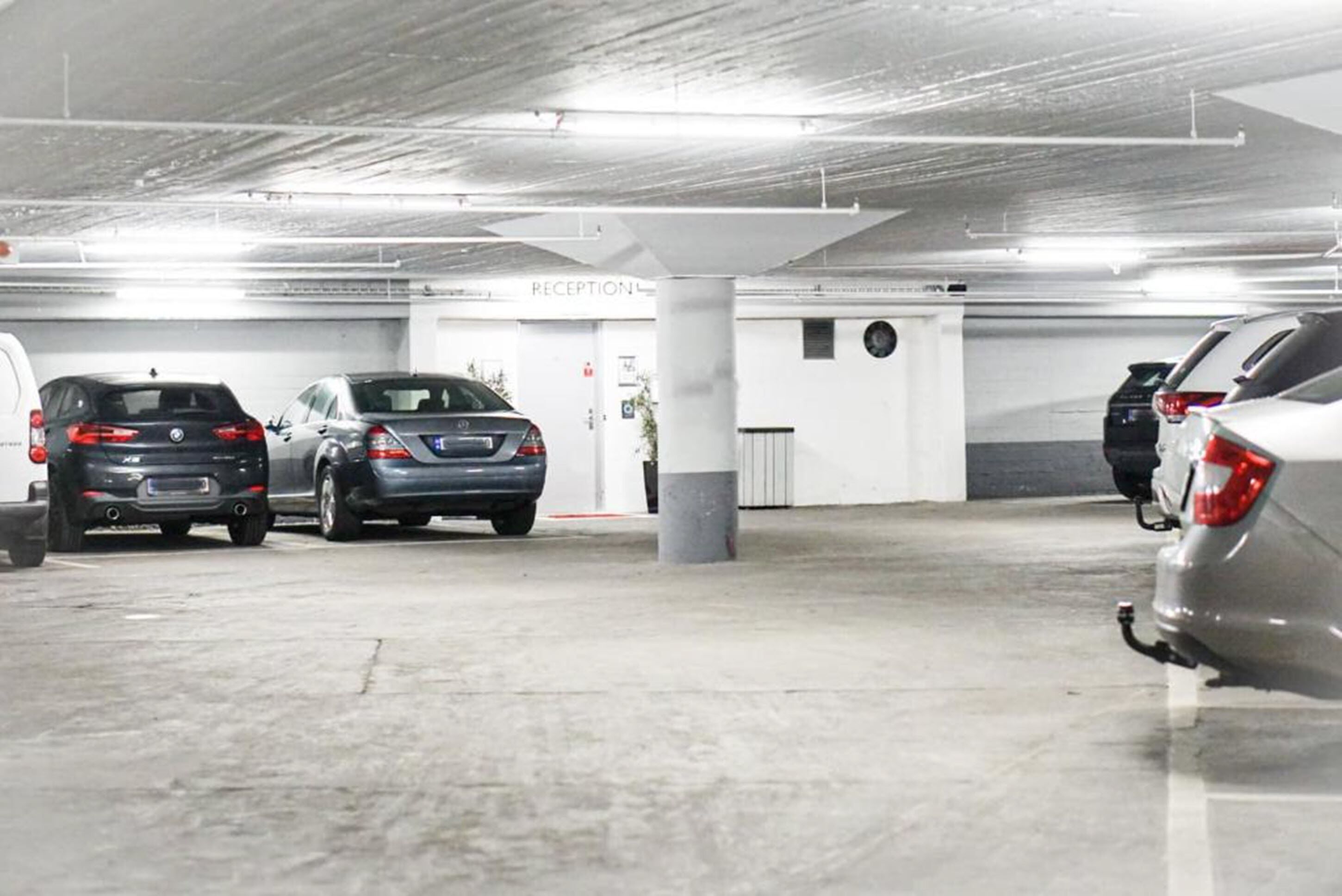 A parking garage with multiple cars parked, a reception area, and a column with a round window.