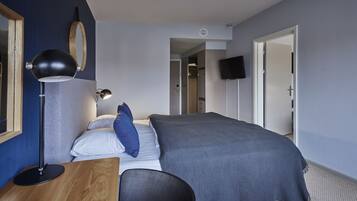 Habitación de hotel con cama, escritorio, lámpara, televisor y armario.