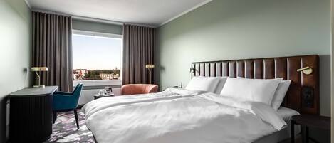 A hotel room with a large bed, a desk, a chair, and a view of the city.