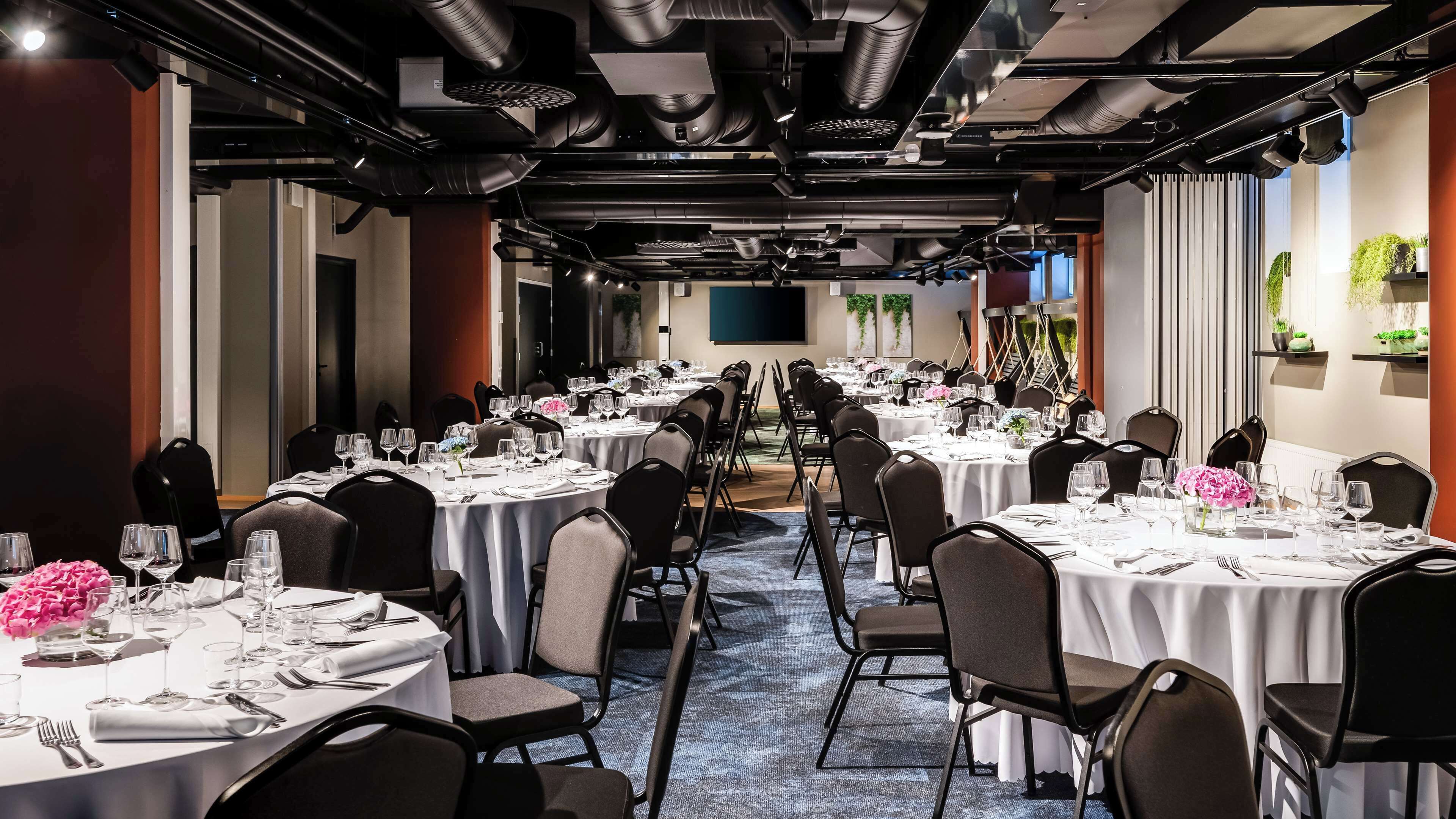 A conference room with multiple round tables, each set with white tablecloths, chairs, and glassware.