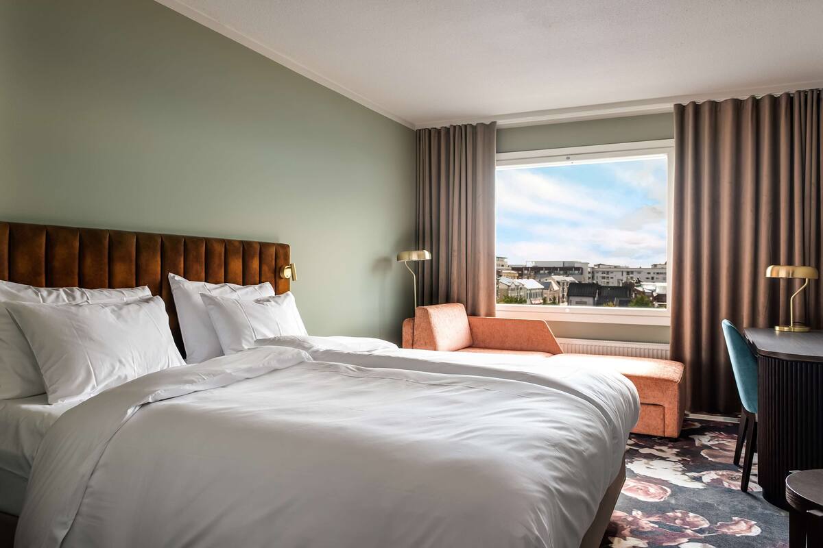 A hotel room with a large bed, a sofa, a desk, and a view of the city.