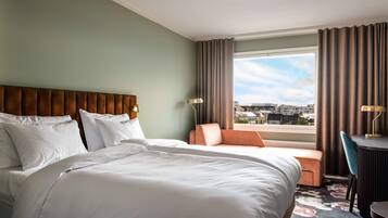 A hotel room with a large bed, a sofa, a desk, and a view of the city.