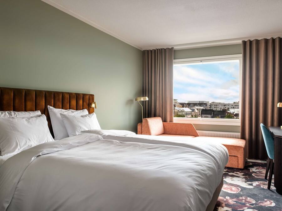 A hotel room with a large bed, a sofa, a desk, and a view of the city.