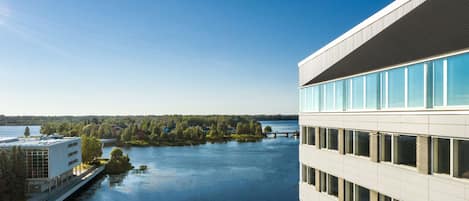Un edificio moderno con fachada de vidrio que da a un río tranquilo y una isla boscosa.