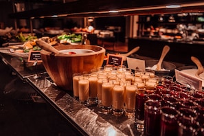 Un bufé con diversos alimentos y bebidas, incluyendo un tazón de madera grande y varios vasos de refrescos.