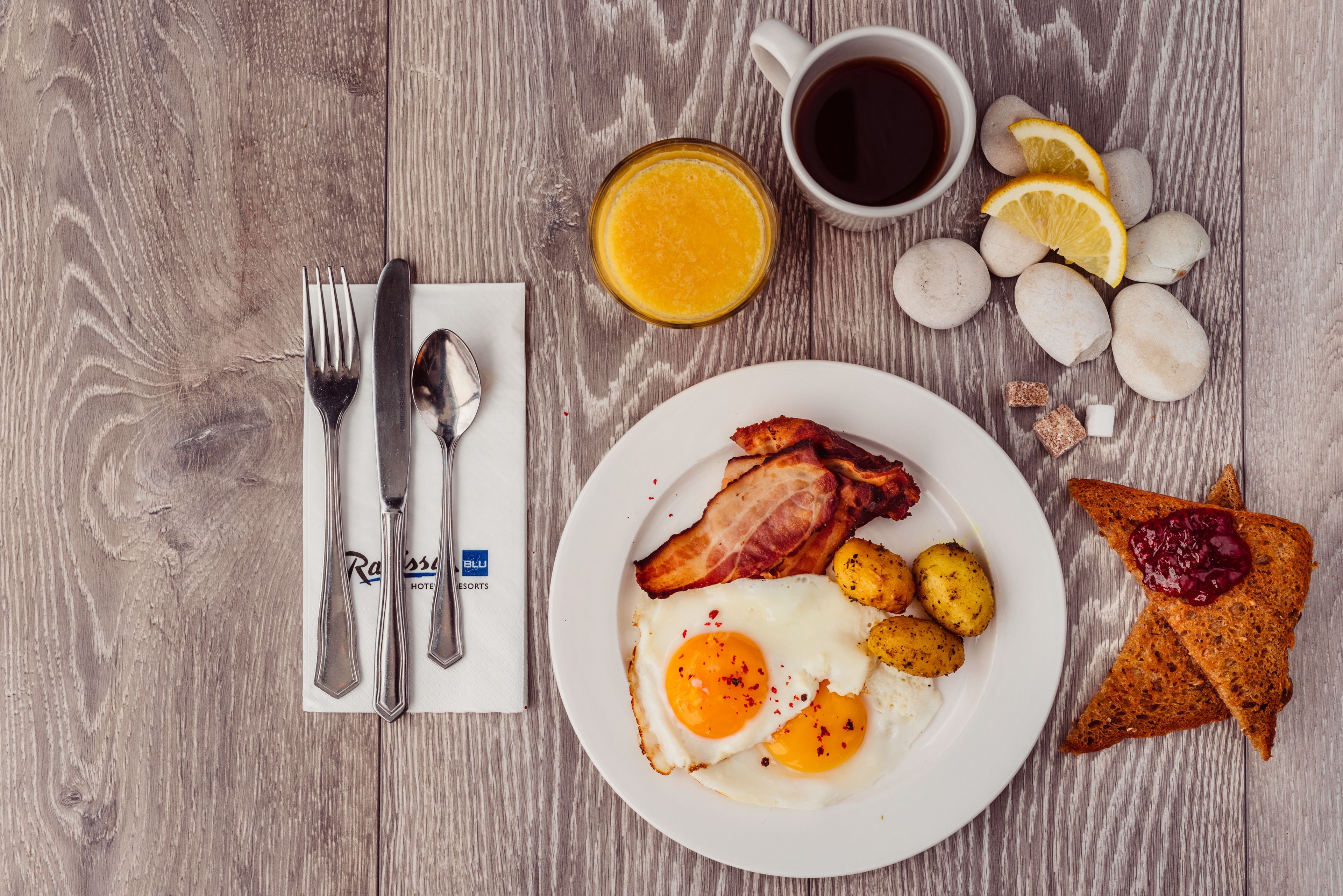 Un plato de desayuno con huevos, tocino, papas, tostadas y jugo de naranja sobre una mesa de madera.