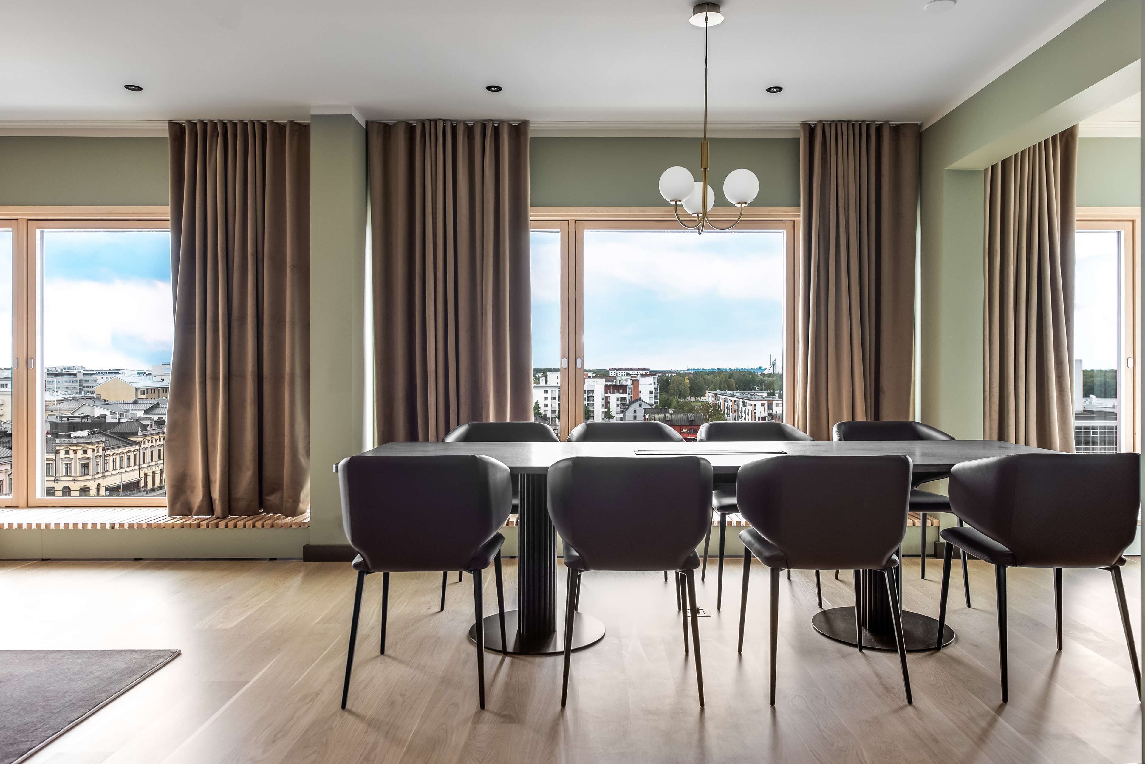 Un espace de restauration moderne avec une grande table et des chaises, de grandes fenêtres avec des rideaux et une vue sur la ville.