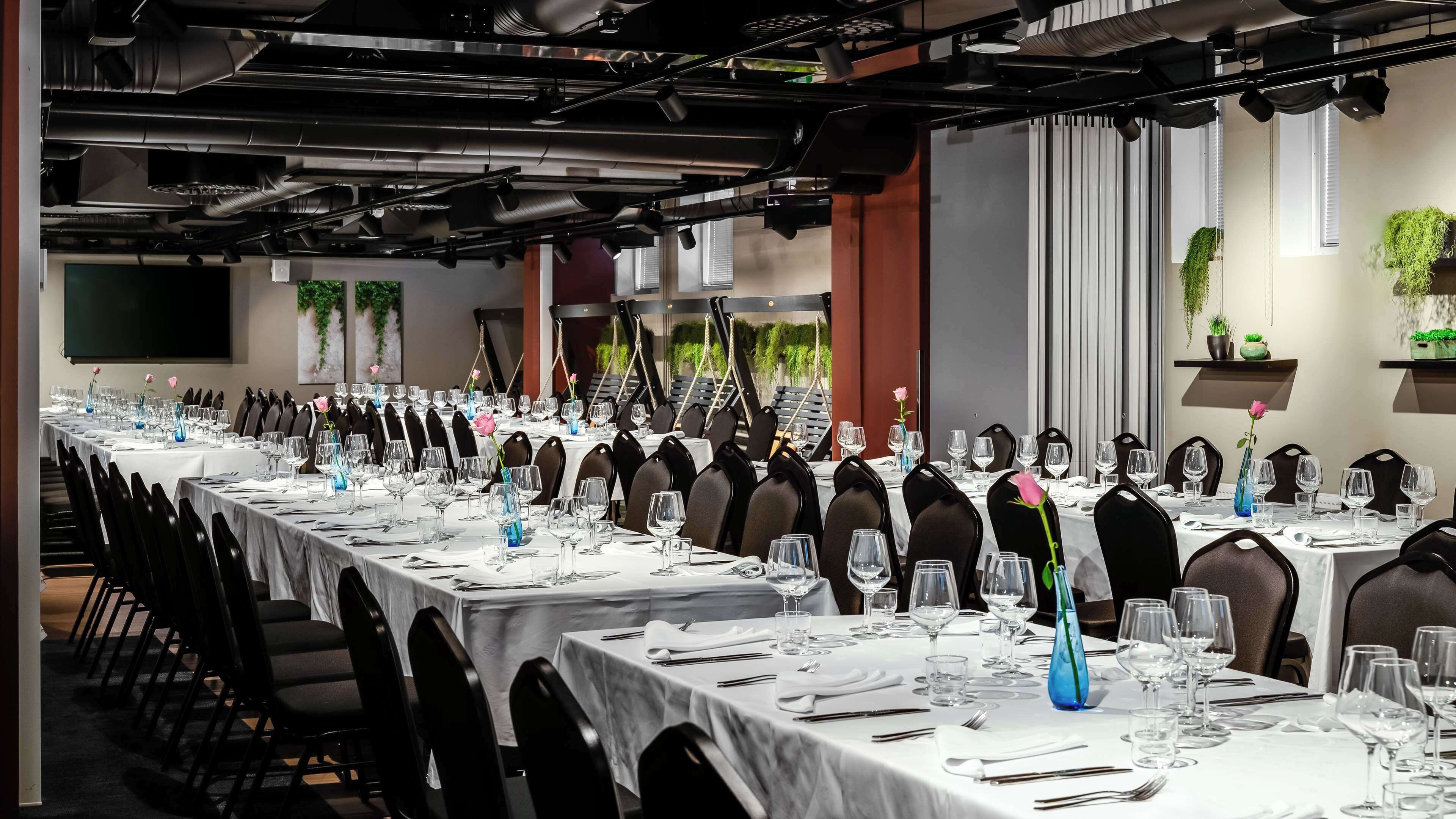 A conference room with long tables set for a formal event, equipped with chairs, tables, and glassware.