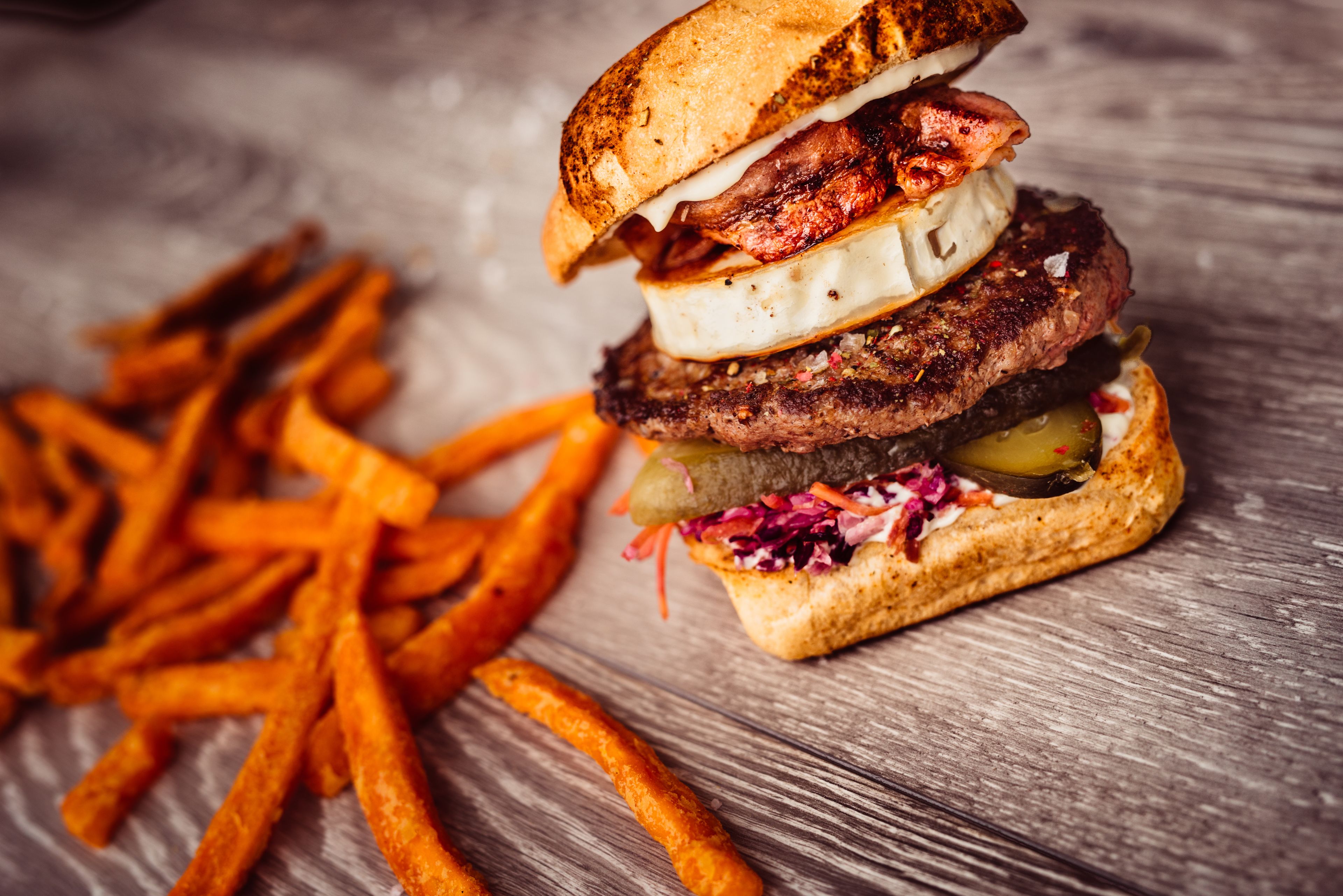 A burger with a toasted bun, lettuce, and pickles on a wooden surface.