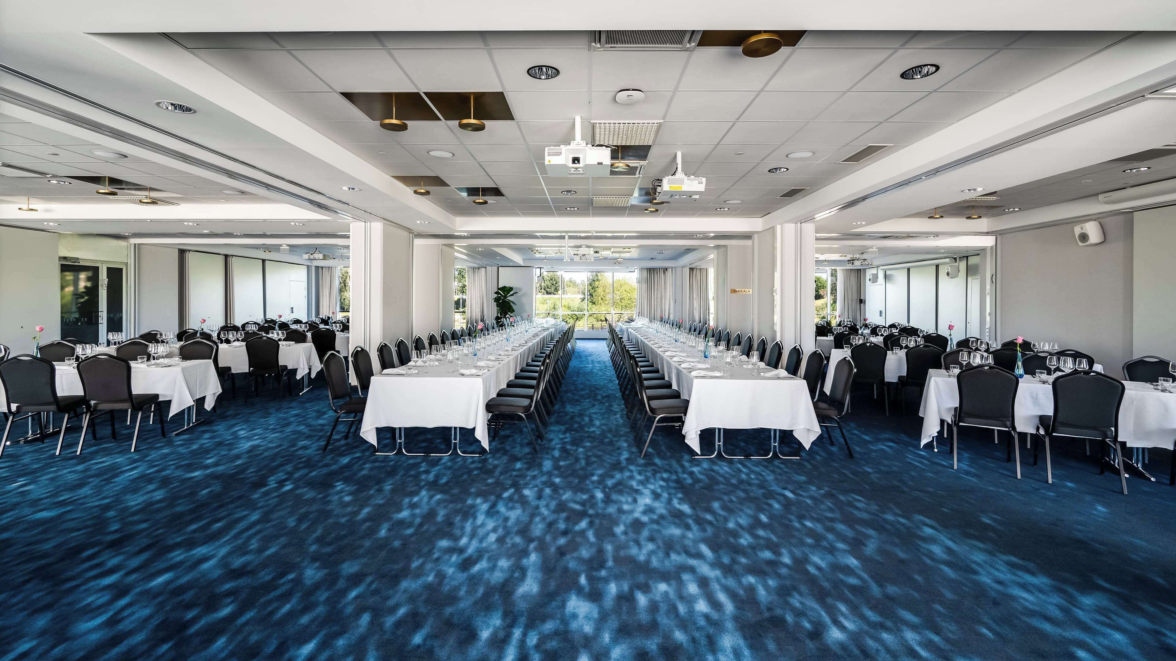 A conference room with long tables, chairs, and a blue carpet.