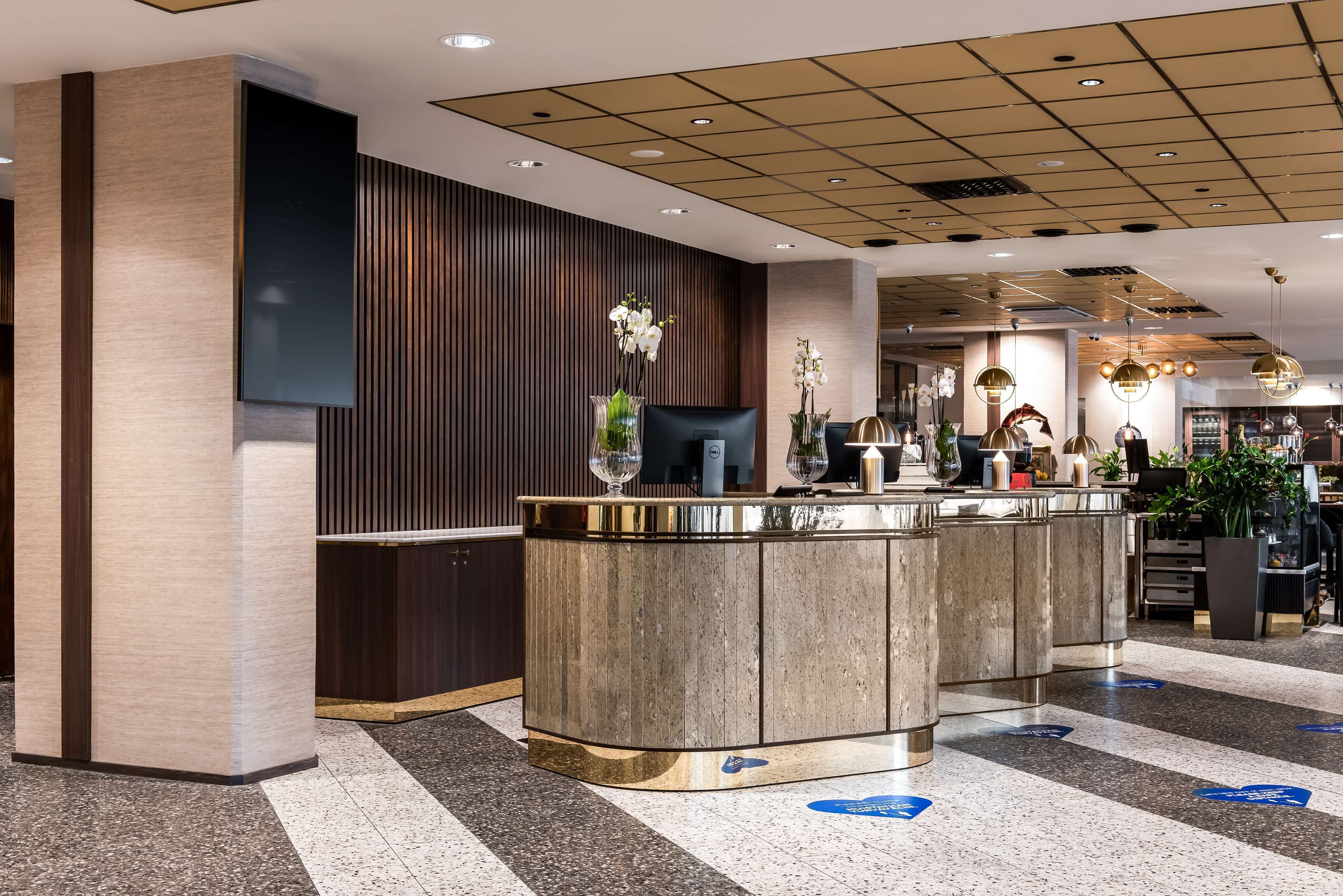 Un espace d’accueil moderne avec un comptoir de réception en bois, un téléviseur à écran plat et une composition florale décorative avec des orchidées.