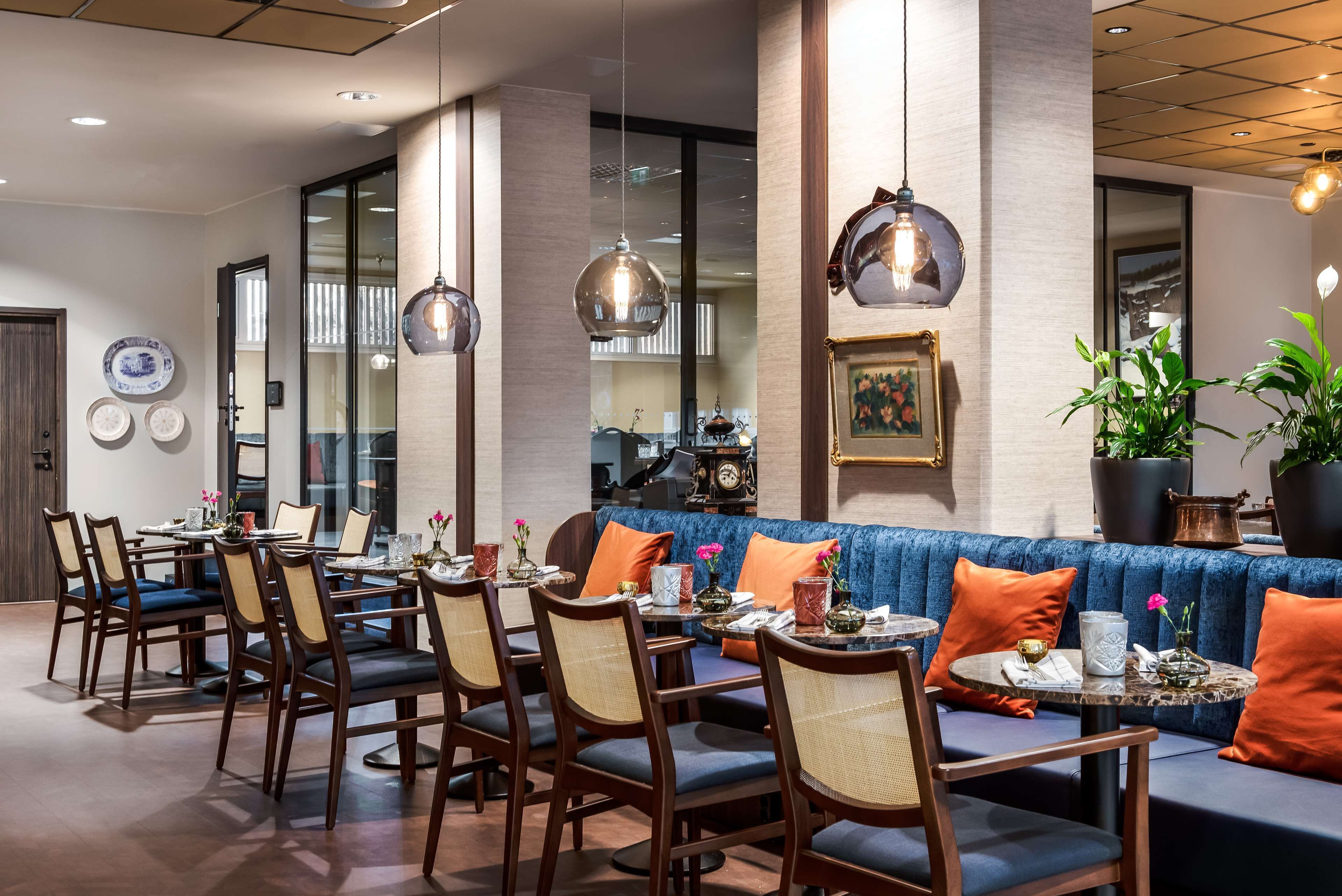 A restaurant with a blue cushioned seating area, wooden chairs, and hanging pendant lights.